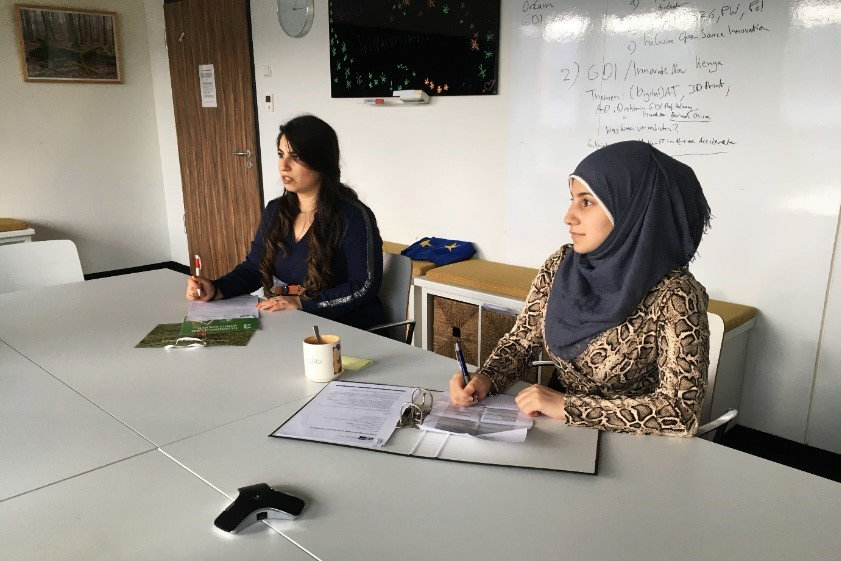 Foto: Zwei Frauen an Tischen in einem Schulungsraum. Beide machen sich Notizen in ihren Unterlagen.