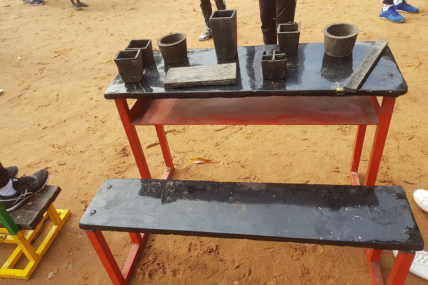 Foto: Auf einem Tisch im Freien stehen verschiedene Gefäße aus Ton. Davor eine Sitzbank.