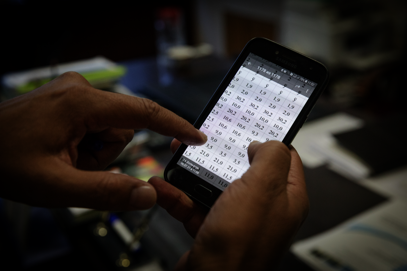 Foto: Hände halten ein Smartphone, auf dem eine Tabelle mit Zahlen zu sehen ist. Der Zeigefinger tippt auf eine Zahl.
