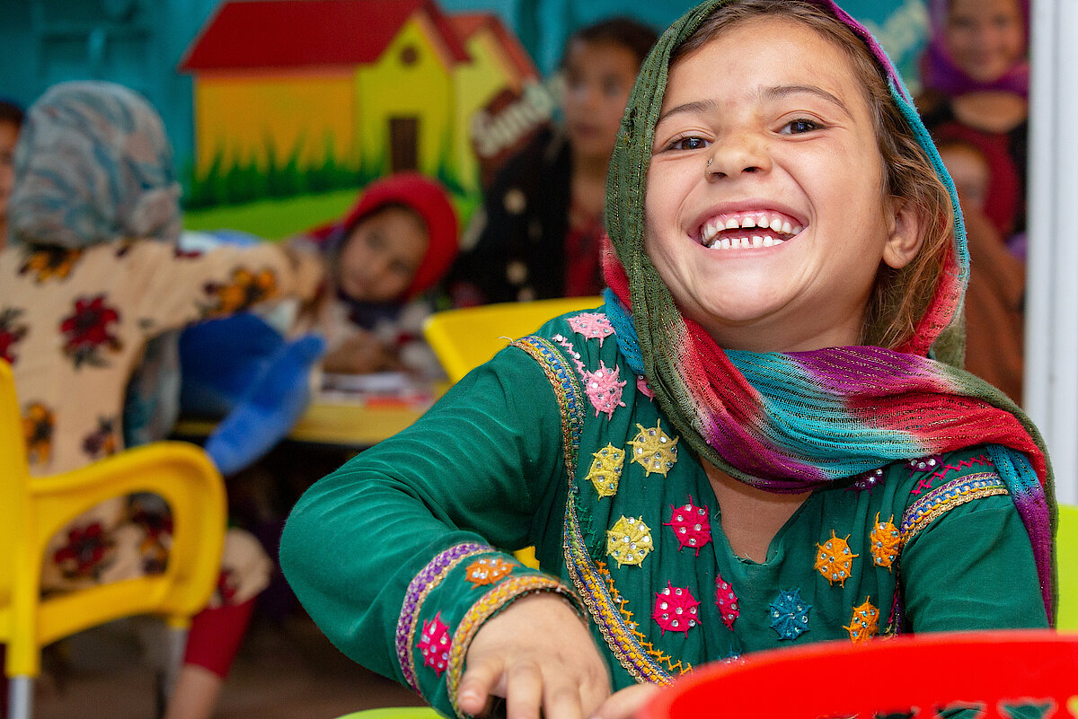 Foto: Ein Mädchen mit buntem Kleid und Tuch lächelt den Betrachter an.