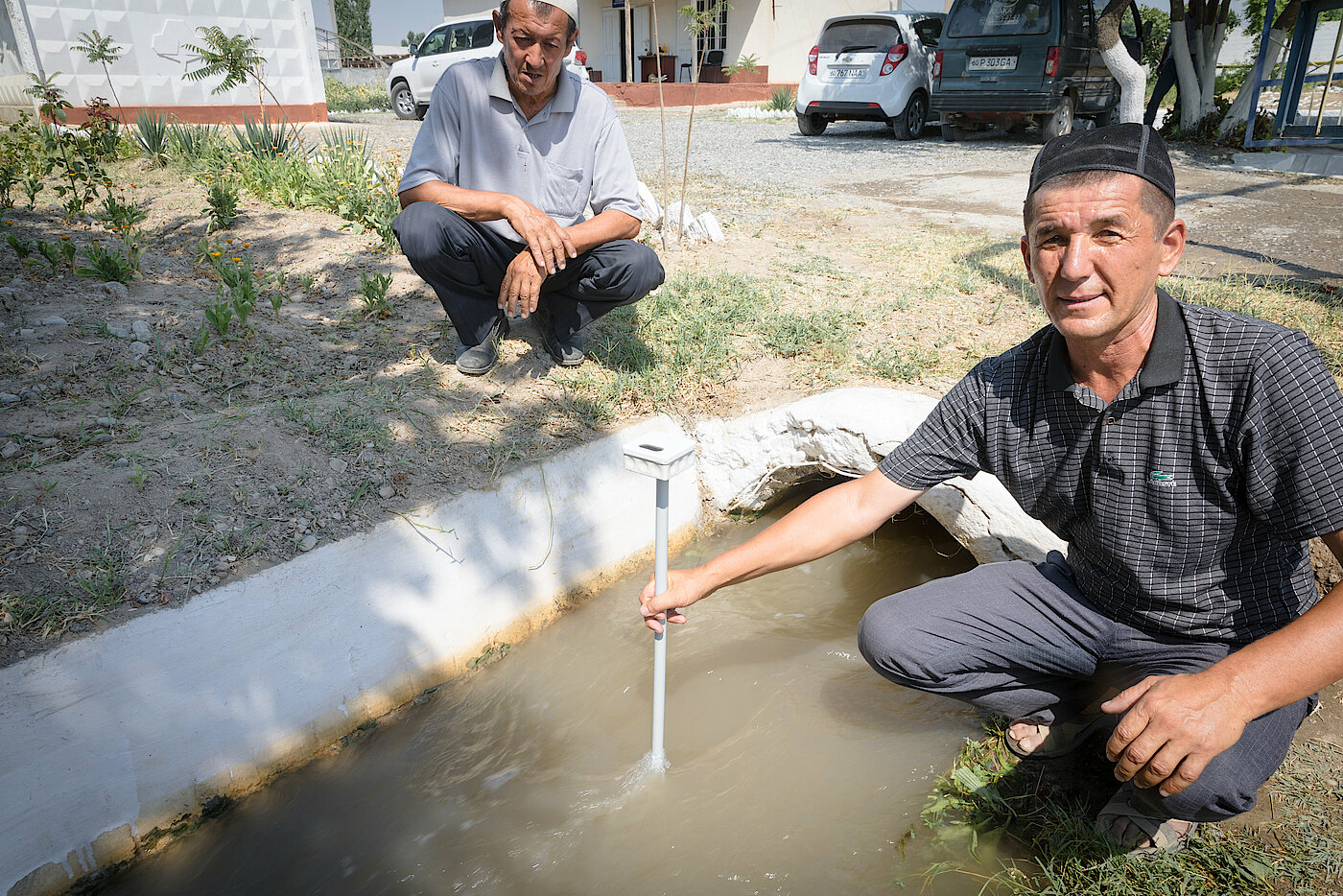Foto: Zwei Männer sind neben einem Wasserlauf. Einer hält ein Wasserstandsmessgerät in das Wasser.