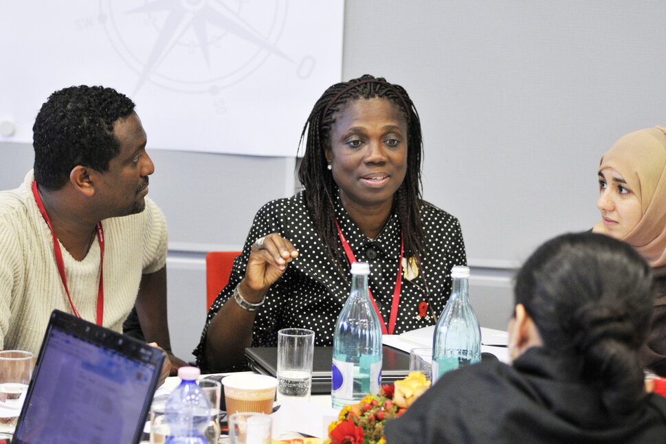 Foto: Der Vorstand der GIZ sitzt an einem Tisch mit Laptops, Unterlagen und Getränken. Eine Frau spricht, die anderen schauen sie an.
