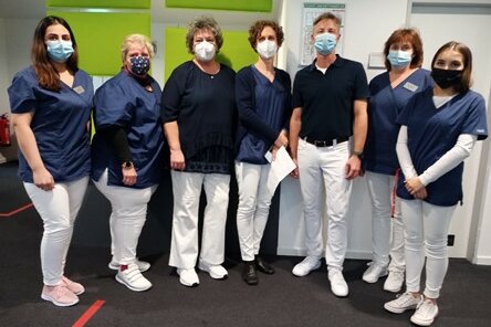 Foto: Sechs Frauen und ein Mann in weißen Hosen, blauen Oberteilen und mit Mundschutz stehen nebeneinander.