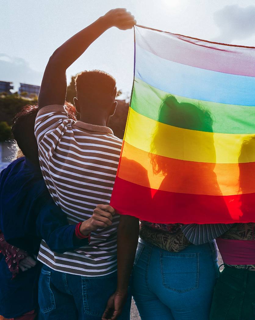 Foto: Mehrere Personen halten hinter sich eine Regenbogenflagge hoch.