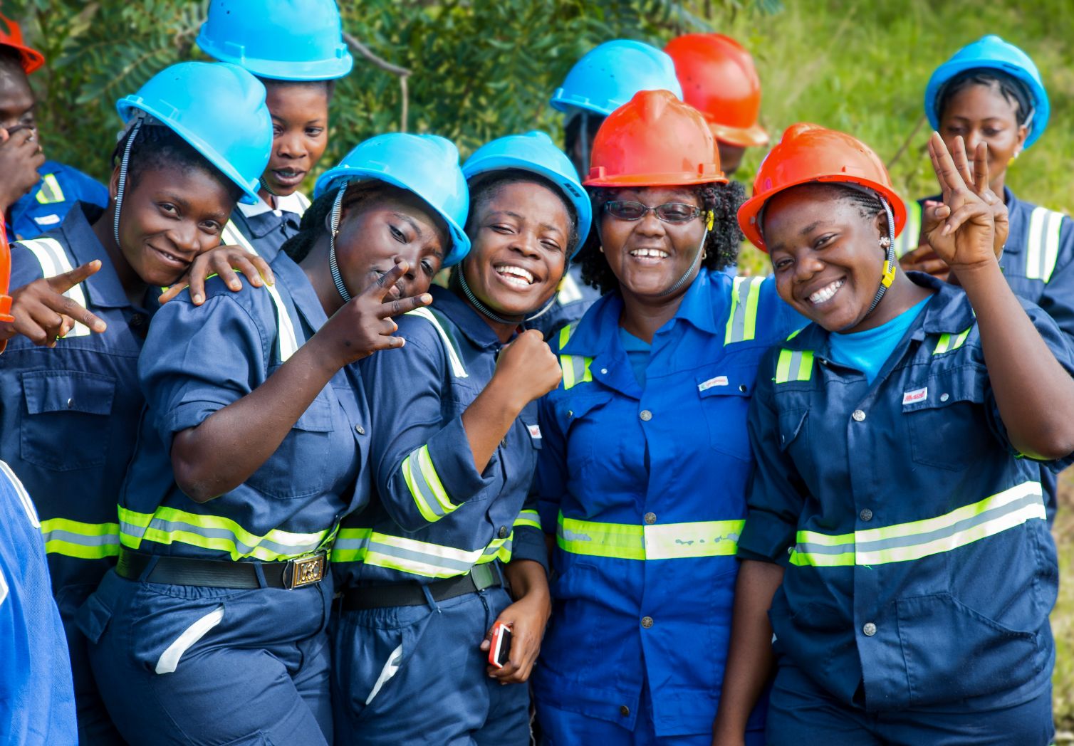 Gruppenfoto: Mehrere Frauen in Arbeitskleidungen und mit Helmen lächeln.