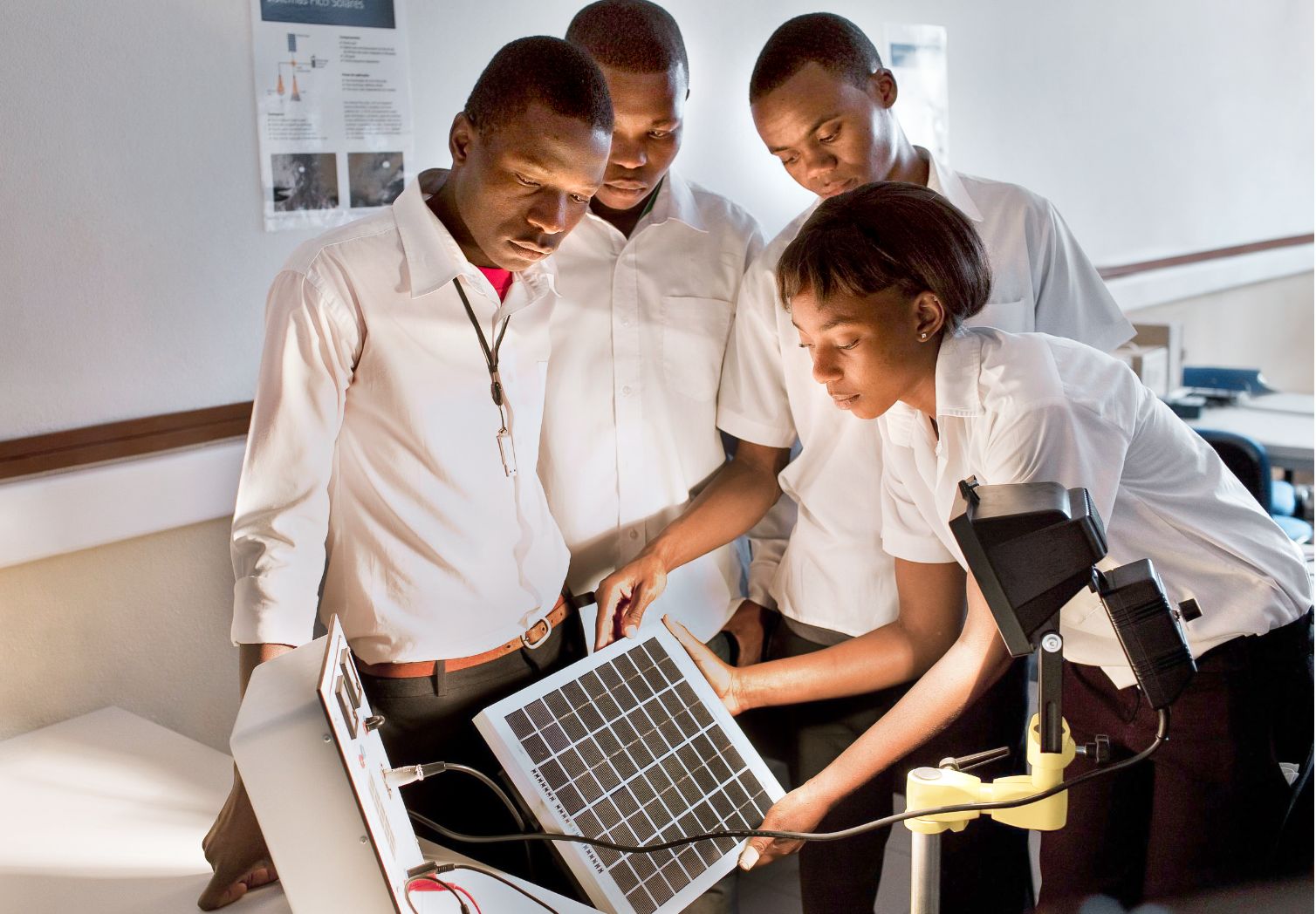 Foto: Vier Personen stehen um ein Solarpaneel, das von einer Lampe angestrahlt wird.