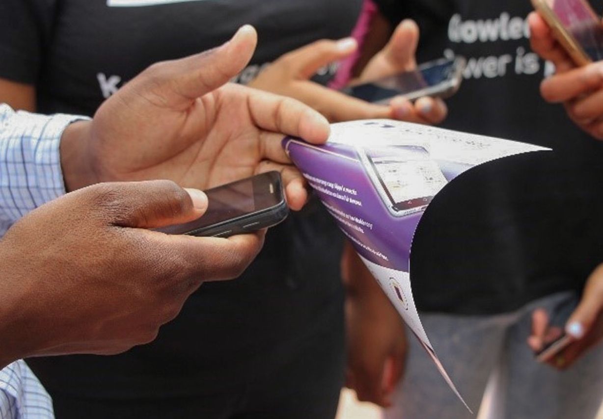 Foto: Zwei Hände halten ein Smartphone und einen Flyer.