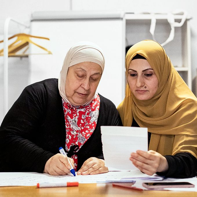 Foto: Zwei Frauen mit Kopftüchern sitzen an einem Tisch und lernen gemeinsam