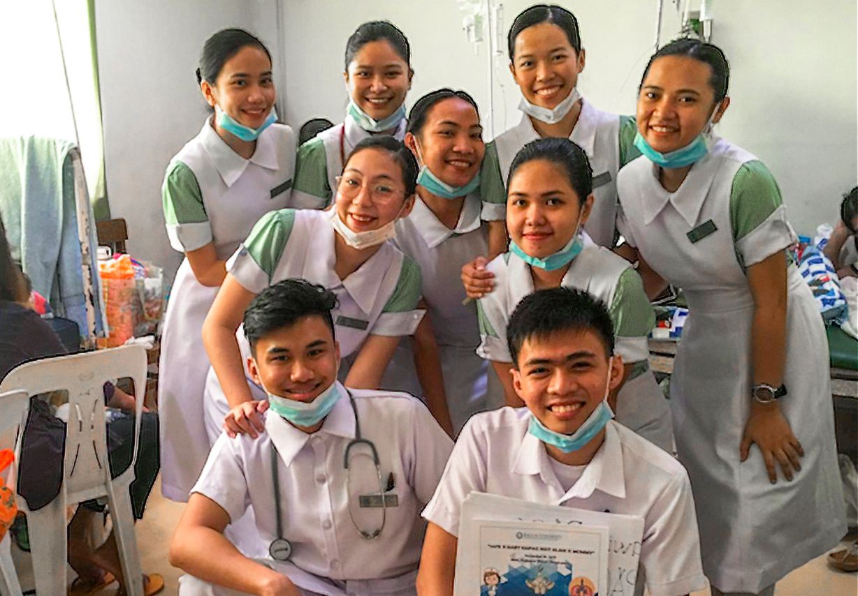 Foto: Sieben junge Frauen und zwei junge Männer in Krankenhauskitteln posieren für ein Gruppenbild.