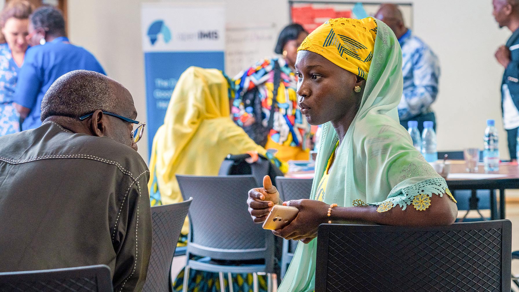 Eine Frau in farbenfroher Kleidung spricht bei einer Veranstaltung in Kamerun mit einem Mann, im Hintergrund weitere Teilnehmende.