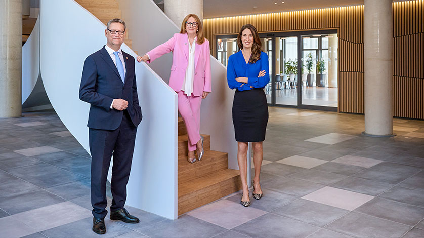 Foto: Ein Mann mit Anzug und Krawatte steht zwischen zwei elegant gekleideten Frauen.