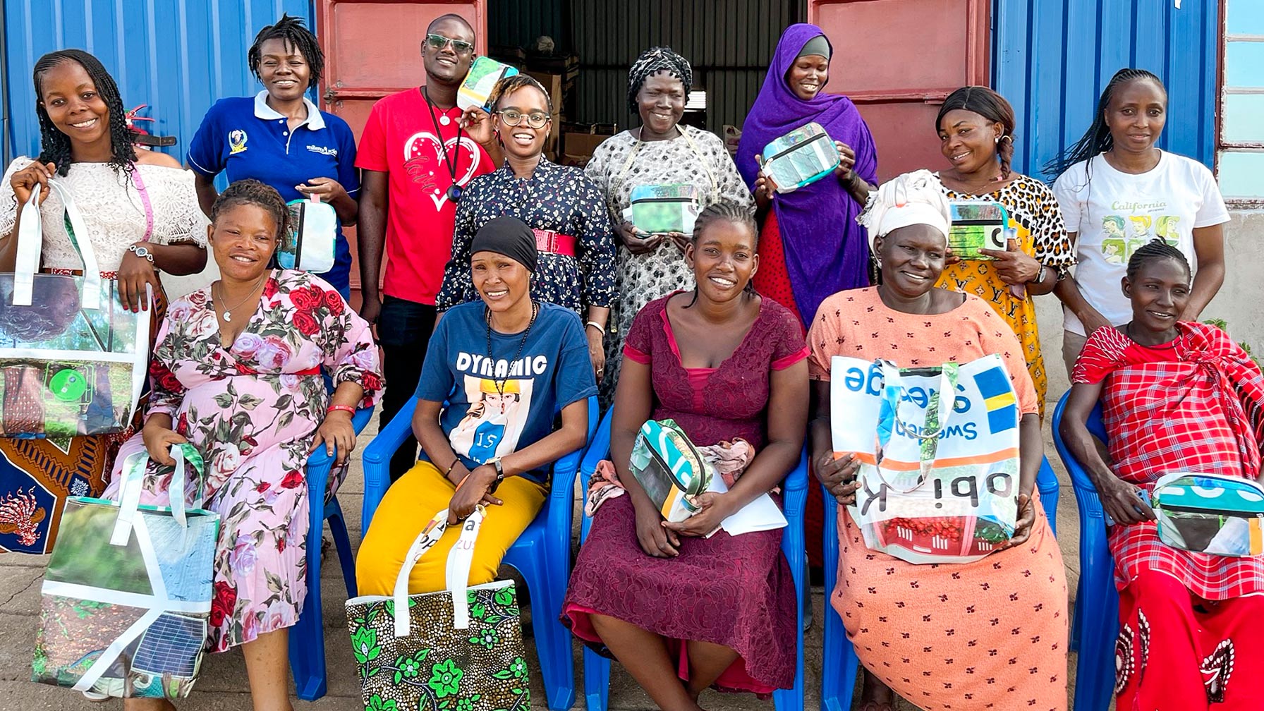 Gruppenfoto von Frauen und Männern vor einem blauen Gebäude, viele halten selbstgenähte Taschen und Beutel aus Recyclingmaterialien.