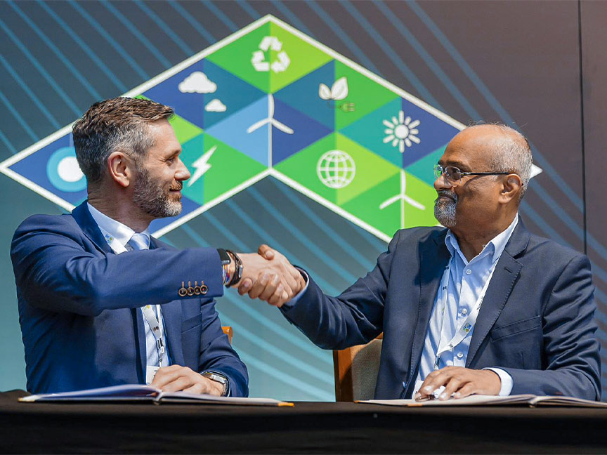 Zwei Männer in Anzügen reichen sich bei der RE-Invest-Konferenz 2024 vor einem Symbolhintergrund die Hand zur Einigung.